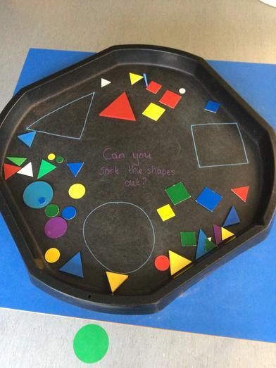 Black tray with colourful geometric shapes for sorting. Includes circles, squares, triangles, and a written question 'Can you sort the shapes out?' 